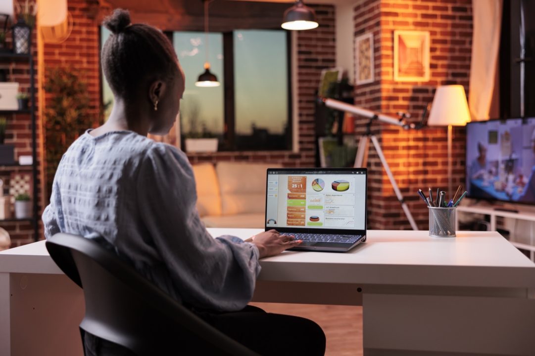 Femme analysant un tableau de bord de données sur son ordinateur portable, le soir, depuis son domicile